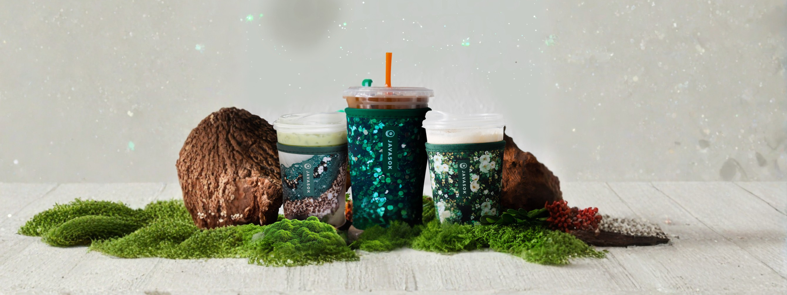 Three insulated cups with lids on a white surface with greenery